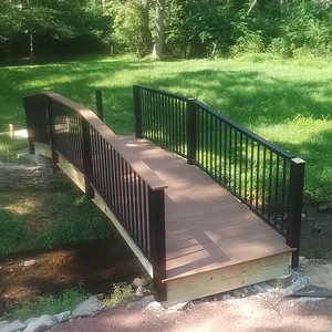 Arched composite footbridge with black aluminum railings crossing the creek in Malvern, PA