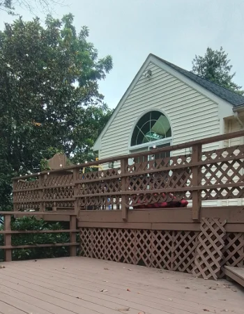 A multi-level brown deck with lattice skirting faces a house with an arched gable window