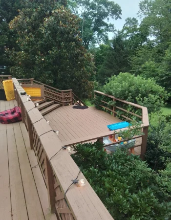 A multi-level brown wooden deck, decorated with string lights, overlooks a dense, green wooded area