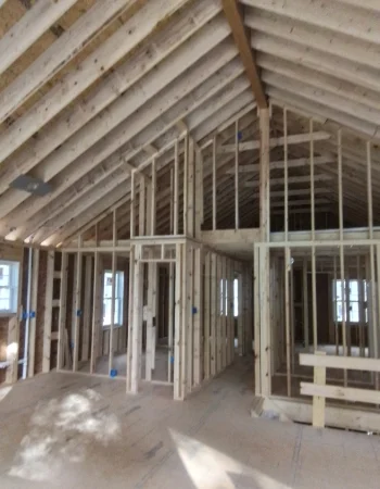 Exposed wood framing reveals the interior structure and vaulted ceiling of a house under construction