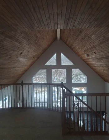 A loft features a sloped wooden ceiling, a dark wood railing, and a large triangular window wall