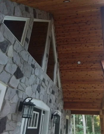 A stone exterior wall meets a wooden ceiling, featuring a vertical bank of triangular windows